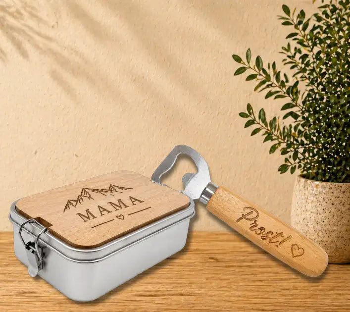 Silberne Metall-Lunchbox mit einem Deckel aus hellem Holz, graviert mit 'mama' und Bergmotiv, begleitet von einem Flaschenöffner mit Holzgriff, beschriftet mit 'prost!'